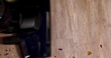 Using a vacuum to efficiently remove colorful confetti from a wooden floor surface video