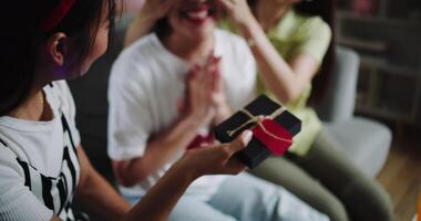 Handheld zoom out shot, One friend blindfolds the birthday person, and the other holds a gift to prepare a surprise in a joyful atmosphere at home. video