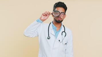 Indian doctor man holds magnifying glass near face looking at camera with big zoomed eye, analyzing video