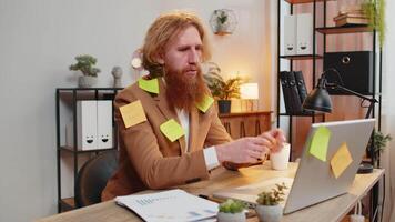 Tired exhausted frustrated businessman sits in home office table with laptop sticky notes many tasks video