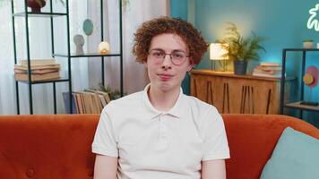 Portrait of happy young Caucasian man sitting on orange sofa looking at camera and smiling at home video