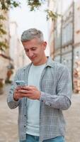 Happy Caucasian man using smartphone typing text messages browsing internet standing on city street video