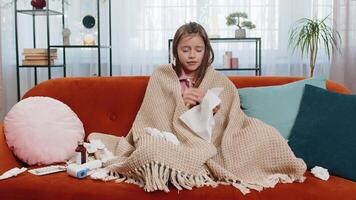 Sick ill girl child suffering from cold flu allergy infection wrapped in blanket sits on home sofa video
