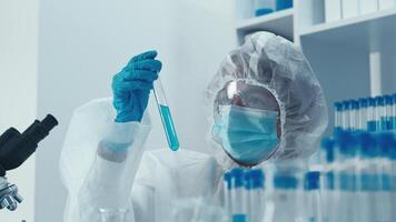 un científico en protector engranaje examina un prueba tubo con brillante azul líquido en un moderno laboratorio, enfatizando el vital papel de investigación, exploración, y avance en Ciencias y tecnología video