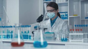 un enfocado científico en un laboratorio Saco examina especímenes utilizando un microscopio, rodeado por vistoso prueba tubos, exhibiendo el precisión y innovación en contemporáneo científico investigación. video