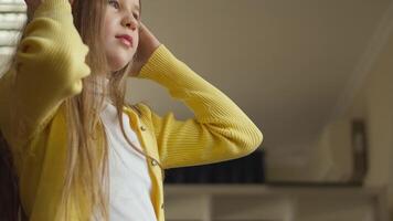 A close-up shows a person wearing a sunny yellow cardigan, a white top, and a patterned skirt, holding an indiscernible object. The indoor setting is cozy, with a bookshelf visible in the backdrop. video