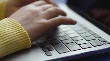 Close-up of hands typing on a sleek, modern laptop. The focus is on the keyboard and the person's hands, which are in motion as they type. A yellow sweater sleeve is visible. video