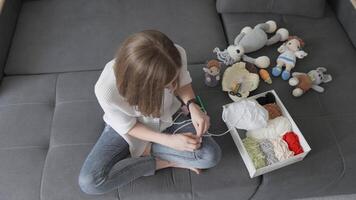 A young woman delights in knitting colorful yarn into whimsical and charming toys, surrounded by an array of playful stuffed animals, which creates a warm atmosphere brimming with creativity and joy video