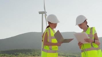 Two skilled female engineers in safety gear are reviewing documents for a wind turbine project, emphasizing teamwork and dedication to advancing renewable energy for a sustainable future video