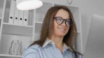 A young woman in glasses smiles while typing on a computer, showcasing a productive and friendly workspace atmosphere. Ideal for themes of remote work, technology, and modern business. video