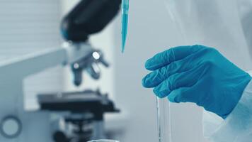 en un bien equipado laboratorio, un experto técnico usos un pipeta a transferir vibrante azul líquido Entre prueba tubos y frascos, demostración precisión en químico análisis y experimentación tecnicas video