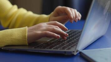 Close-up of hands typing on a laptop keyboard. A person wearing a yellow sweater works on a laptop with a bright blue surface. The image conveys a sense of productivity or communication. video