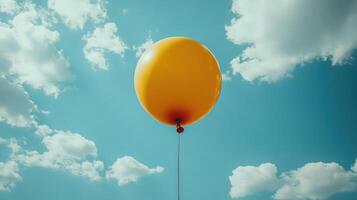 Bright yellow balloon floats against a clear blue sky with fluffy white clouds during a sunny day photo