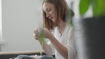 A woman enjoys a tranquil moment at home, deeply engaged in her knitting while basking in warm light filtering through vibrant greenery. This scene captures mindfulness and creativity in every stitch video