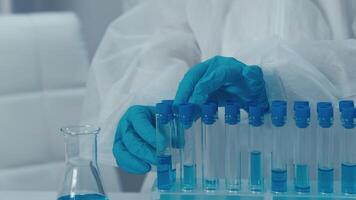 en un ocupado laboratorio lleno con equipo, un experto investigador cuidadosamente manejas prueba tubos con vibrante azul líquidos, demostrando precisión y pericia en conductible complejo científico experimentos video