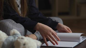 A young person, likely a student, sits comfortably with a notebook on a floor. The person wears long sleeves and patterned trousers. A stuffed animal rests close by, adding to the cozy, intimate setting. video