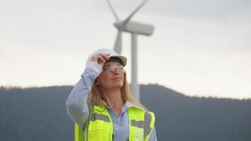 A skilled female engineer in a bright safety vest and hard hat stands confidently in front of a large wind turbine, symbolizing the future of innovative renewable energy solutions video