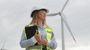 A female engineer, dressed in bright reflective gear, stands confidently beside a towering wind turbine, representing the essence of innovation and dedication within the field of renewable energy video