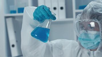 en un lo último laboratorio, un dedicado científico en protector engranaje examina un vaso matraz con un vibrante azul solución, exhibiendo el precisión y atención vital para seguro experimentos video