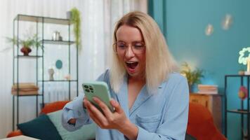Excited amazed winner young woman freelancer using smartphone receive email message win online game video