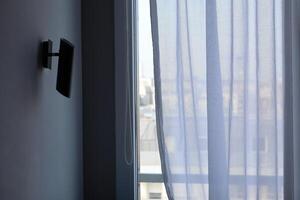 Soft curtains gently sway in the breeze, revealing a sunlit city view from an indoor space photo