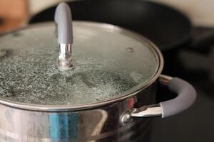 Cooking a pot of water on a stovetop with steam forming under the lid in a kitchen setting photo