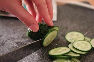 Chopping fresh cucumber into slices on a cutting board in a cozy kitchen during daylight hours photo