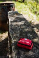 A bright red first aid kit is resting on a sturdy wooden bench, creating a vivid contrast against the natural tones of the wood. It is a useful item in case of any emergencies photo