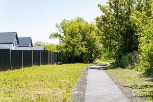 A picturesque path that meanders through a lush grassy field, adorned with beautiful trees and serene houses visible in the background, creating a peaceful atmosphere for walking photo