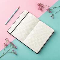 Open notebook with grid pages on pastel pink and blue background with flowers and pencil in vibrant arrangement and copy space photo
