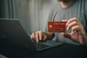 Close-up Man hand Holding Credit Card While Using Laptop for Online Transactions in Modern Setting, Demonstrating E-Commerce and Digital Payment Safety photo