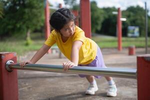 Asian Young girl practicing strength training on playground equipment in a sunny park, focusing on fitness and outdoor activities with determination and joy. photo