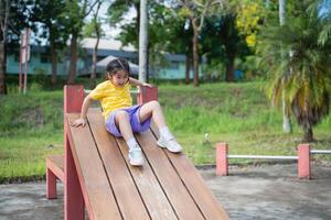 Asian Young child enjoying a sunny day at the playground, sliding down a wooden play structure, laughter and joy captured in outdoor playtime fun photo