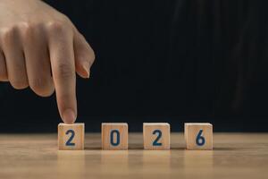 Hand arranging wooden blocks with numbers 2026 on a wooden surface symbolizing the approaching year and new beginnings for future planning and aspirations photo