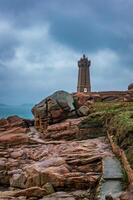 a lighthouse on a rocky shore with a dark sky photo