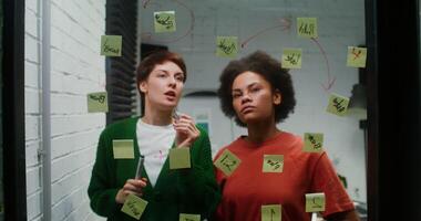 Two women standing in front of a window with sticky notes on it photo
