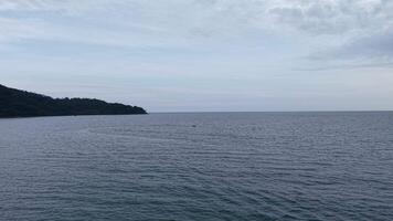 Drone shot of a quiet beach with soft waves and forested hills stretching along the coastline. video