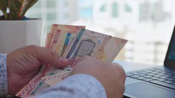 A man holding a bundle of money in front of a laptop video