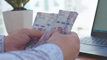 A person holding a bundle of money in front of a laptop video