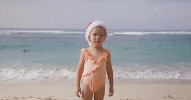 Cute little girl playing in ocean beach with Christmas hat. Happy winter vacation in tropics video