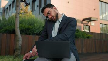 Caucasian busy man multitasking businessman working with laptop computer outdoors writing notes in notebook paperwork business commerce male office manager talk mobile phone online consulting in city video
