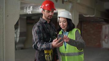 dois multiétnico construtores usando Móvel telefone construção Projeto aplicativo mostrando polegar acima japonês mulher caucasiano homem capacete de segurança engenheiros o negócio inspetor navegando Smartphone verde tela zombar acima gostar aprovar video