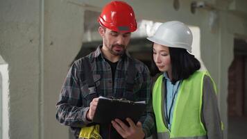 multiétnico construtores uniforme assinatura construção contrato prancheta caneta placa acordo caucasiano homem japonês mulher o negócio escrevendo assinatura documento Construir arquitetos dois engenheiros relatório inspeção às local video