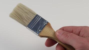 Hand holding a paintbrush preparing for artwork at an indoor workspace with a clean backdrop video