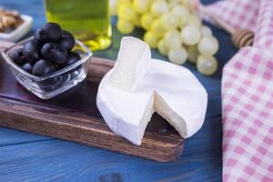 appetizer camembert cheese with olives on a wooden board with honey and grapes on a blue background photo