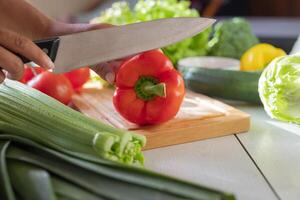 Girl cook in the kitchen slicing red bell pepper with a knife preparing fresh vegetables for a meal photo