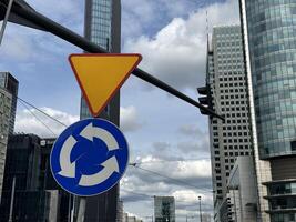 Warsaw, Poland - May 22, 2025 Traffic sign indicating roundabout with modern skyscrapers in the background, showcasing urban architecture and city life in a bustling metropolitan area photo