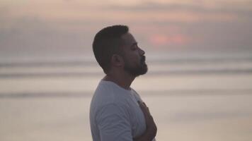 Brown Beard Asian man practices breath control at sunset on the beach. A quiet moment of healing, mindfulness, emotional grounding, and inner peace video