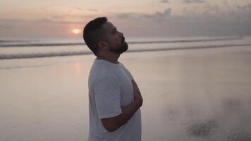 Brown Beard Asian man practices breath control at sunset on the beach. A quiet moment of healing, mindfulness, emotional grounding, and inner peace. video