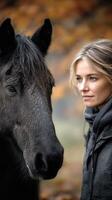 Woman interacts with a black horse in a serene autumn landscape surrounded by golden leaves photo